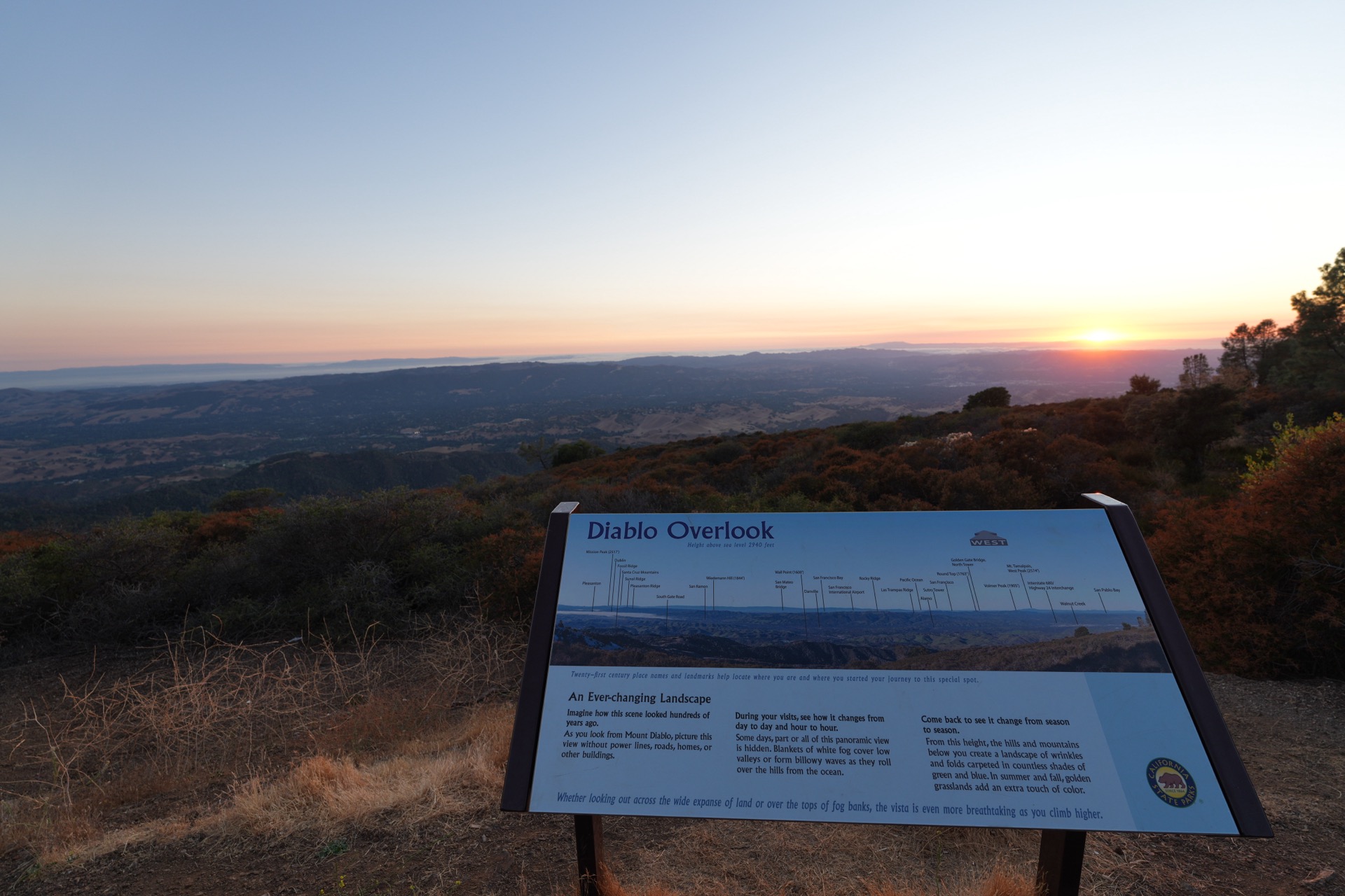 The Diablo Overlook interpretive sign in the foreground, the sun glowing orange behind the hills in the background
