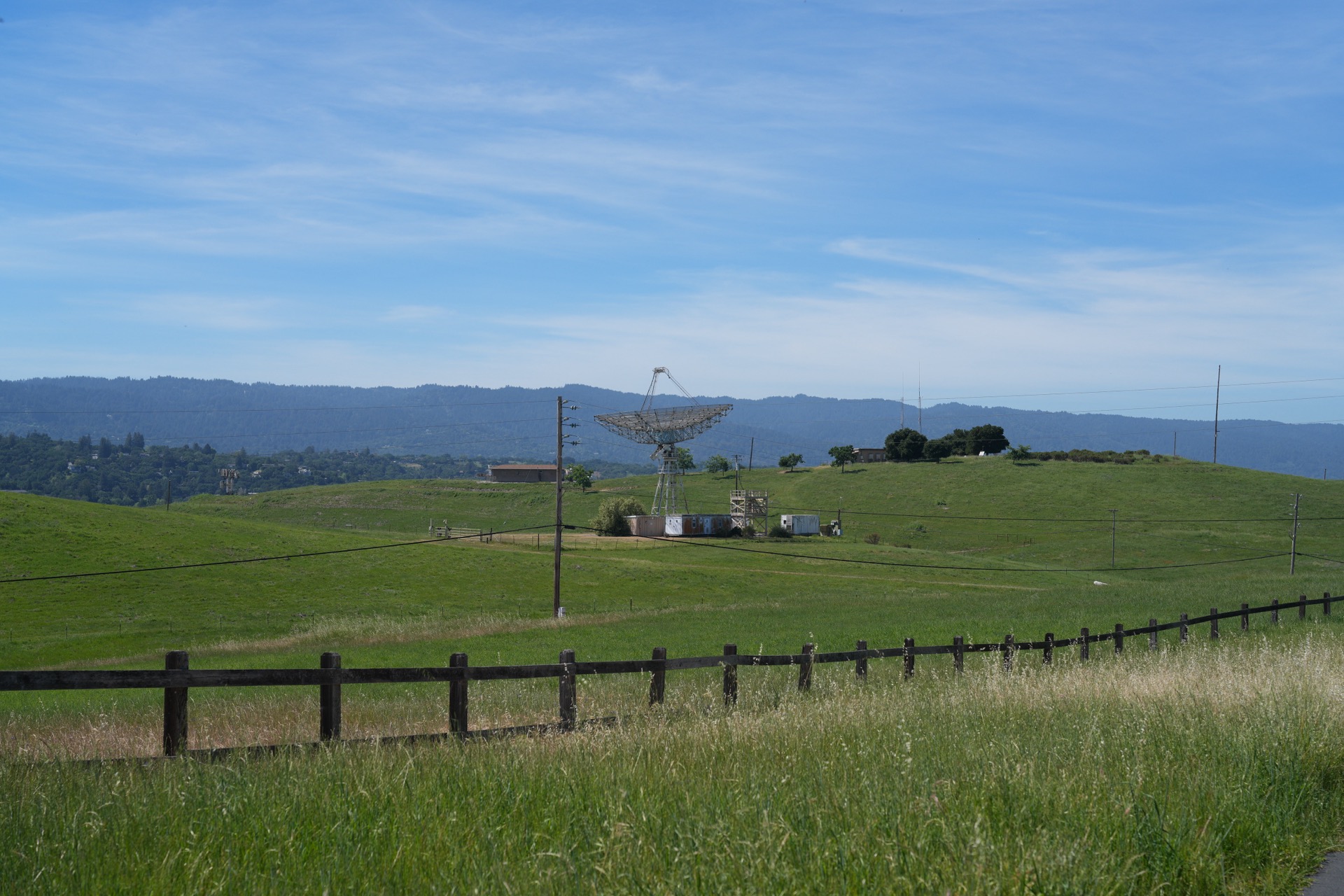 The Stanford Dish radio telescope across a wide green valley, surrounded by rolling hills and fencing