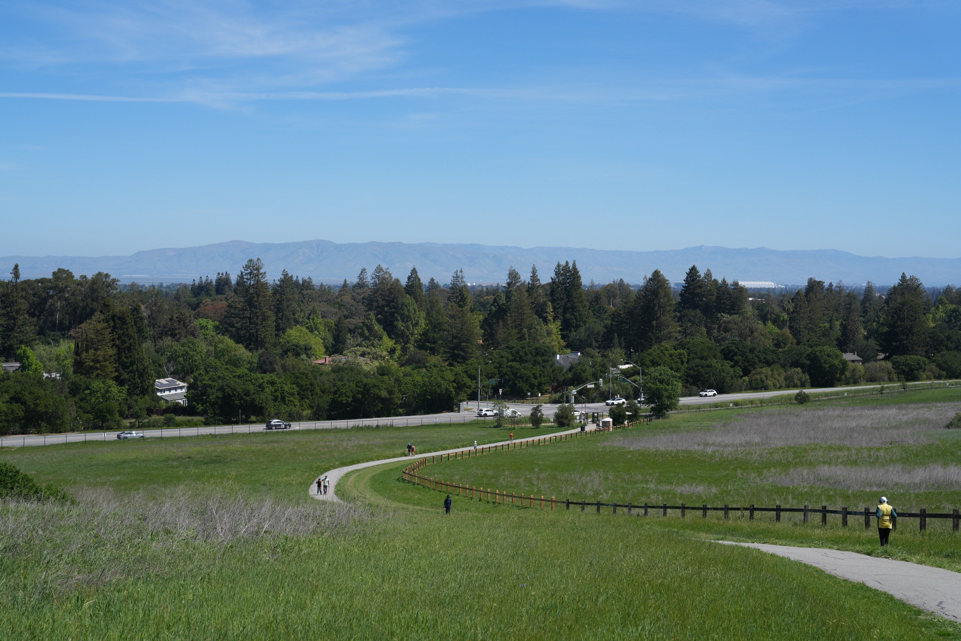 The paved winding trail through rolling green hills, a few distant hikers visible along the ridge